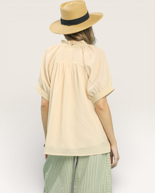 Woman wearing a beige top and straw hat on a plain background