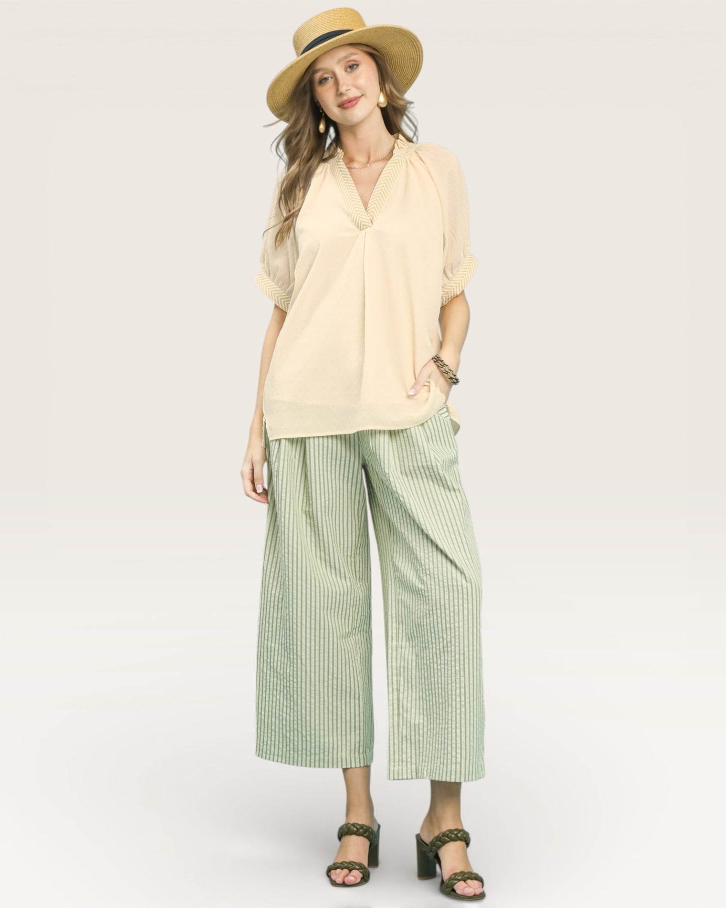 Woman wearing a beige blouse and green checkered pants with a straw hat on a white background