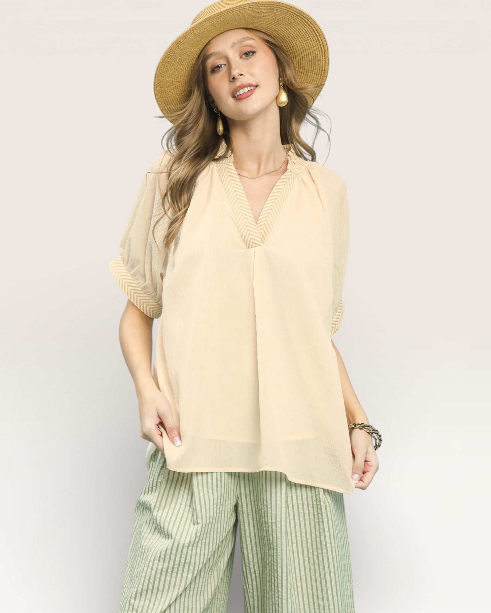 Woman wearing a beige blouse, green striped pants, and a straw hat on a white background