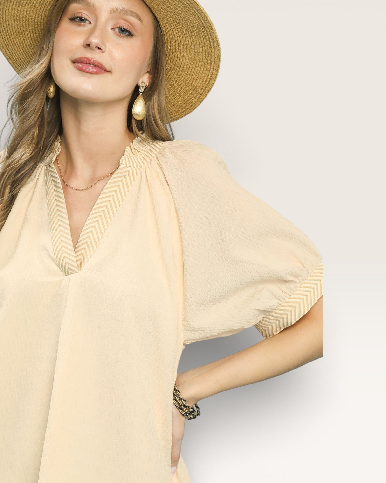 Woman wearing a beige blouse and straw hat on a plain background
