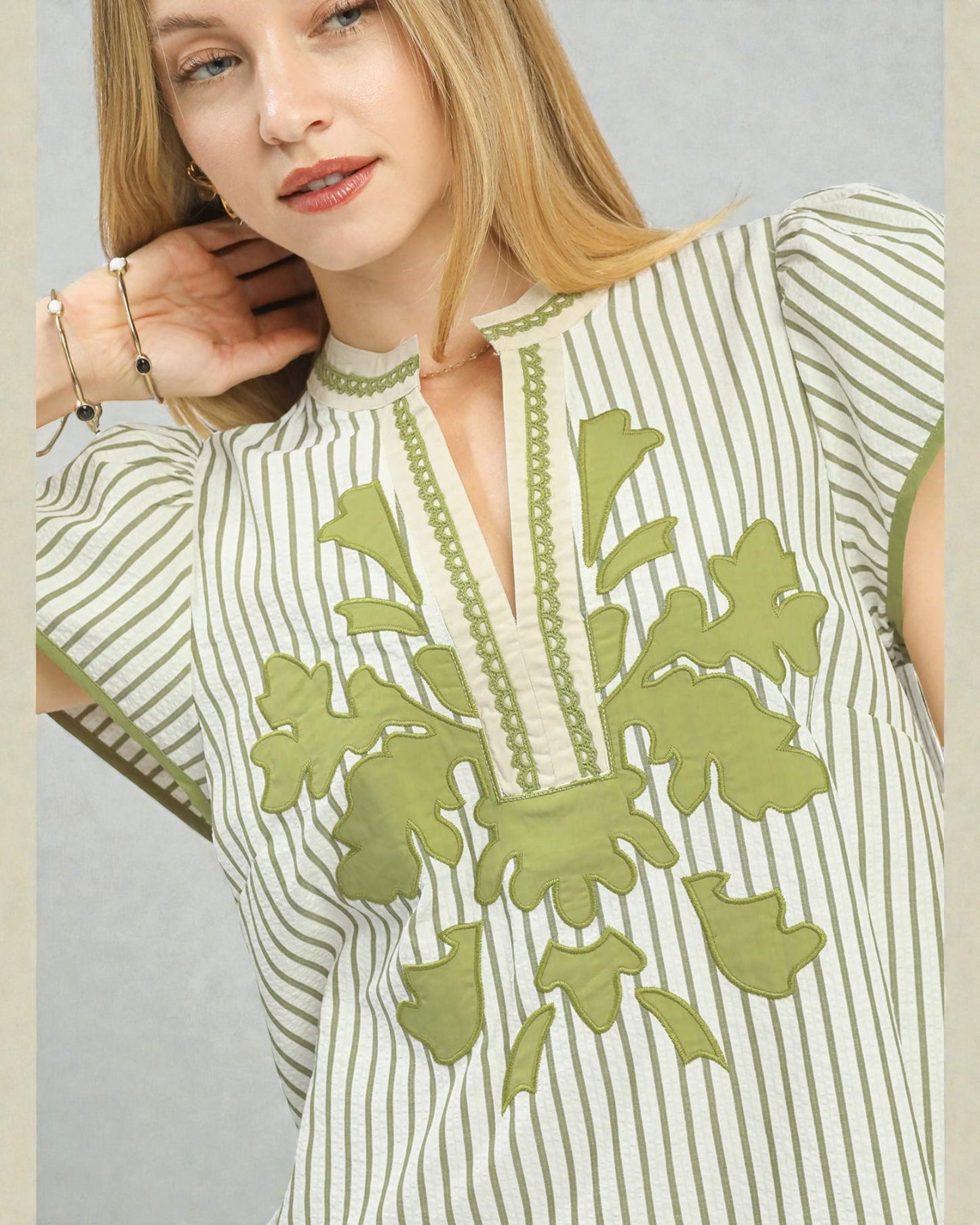 Woman wearing a green and white striped top with floral embroidery on a gray background