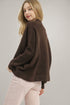 Woman wearing a brown sweater and light pink pants against a plain background