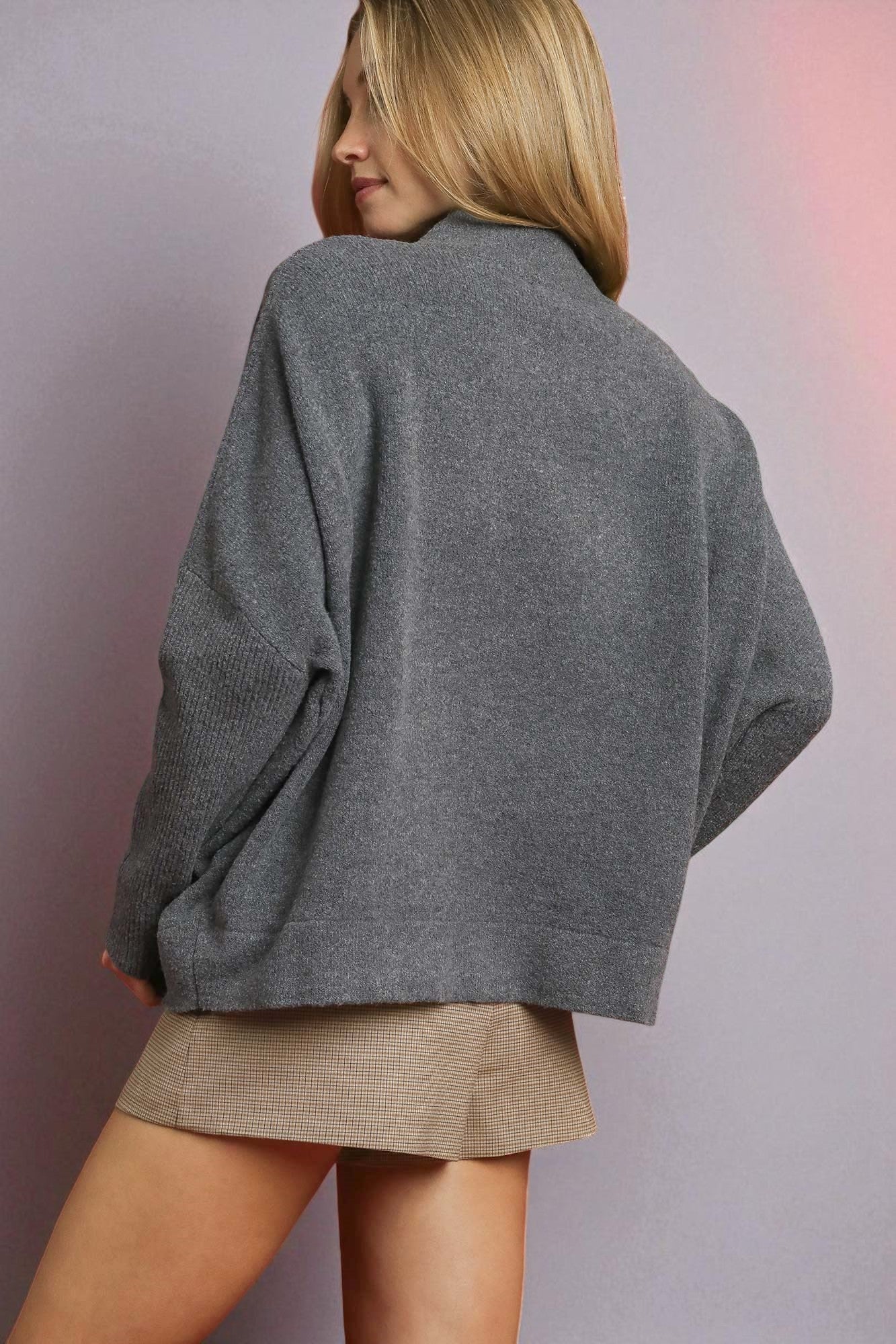 Person wearing a gray sweater and beige skirt against a plain background