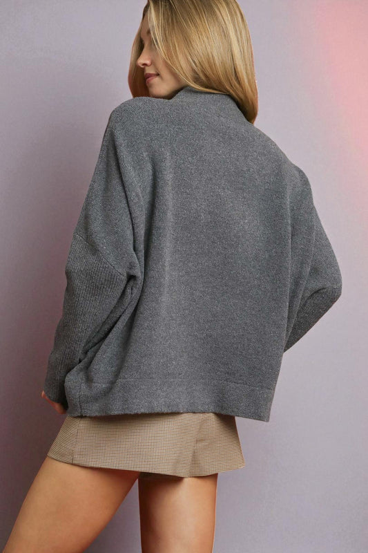 Person wearing a gray sweater and beige skirt against a plain background