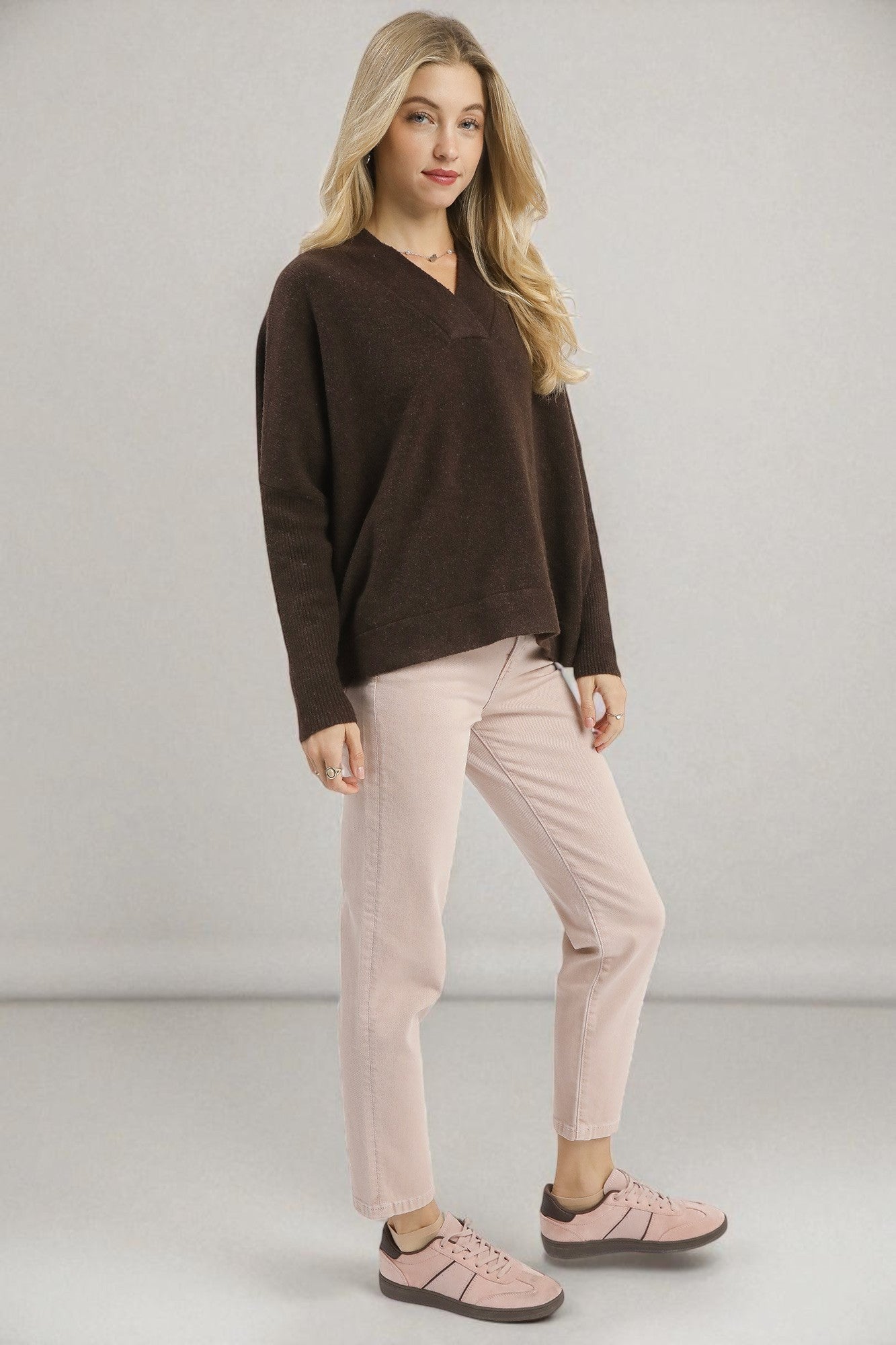 Woman wearing a brown sweater and pink pants against a plain background