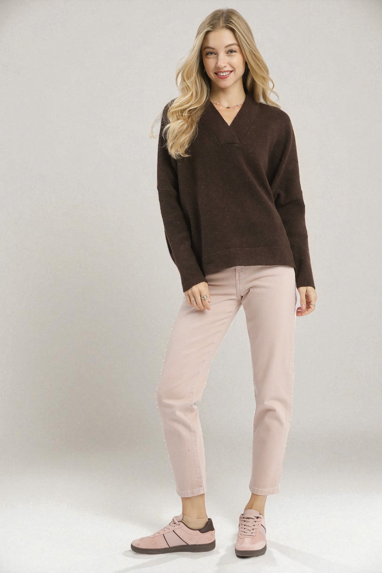 Woman wearing a brown sweater and pink pants against a white background