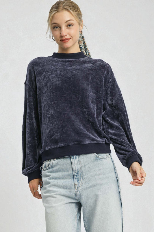 Woman wearing a dark blue velour sweater and light blue jeans on a white background