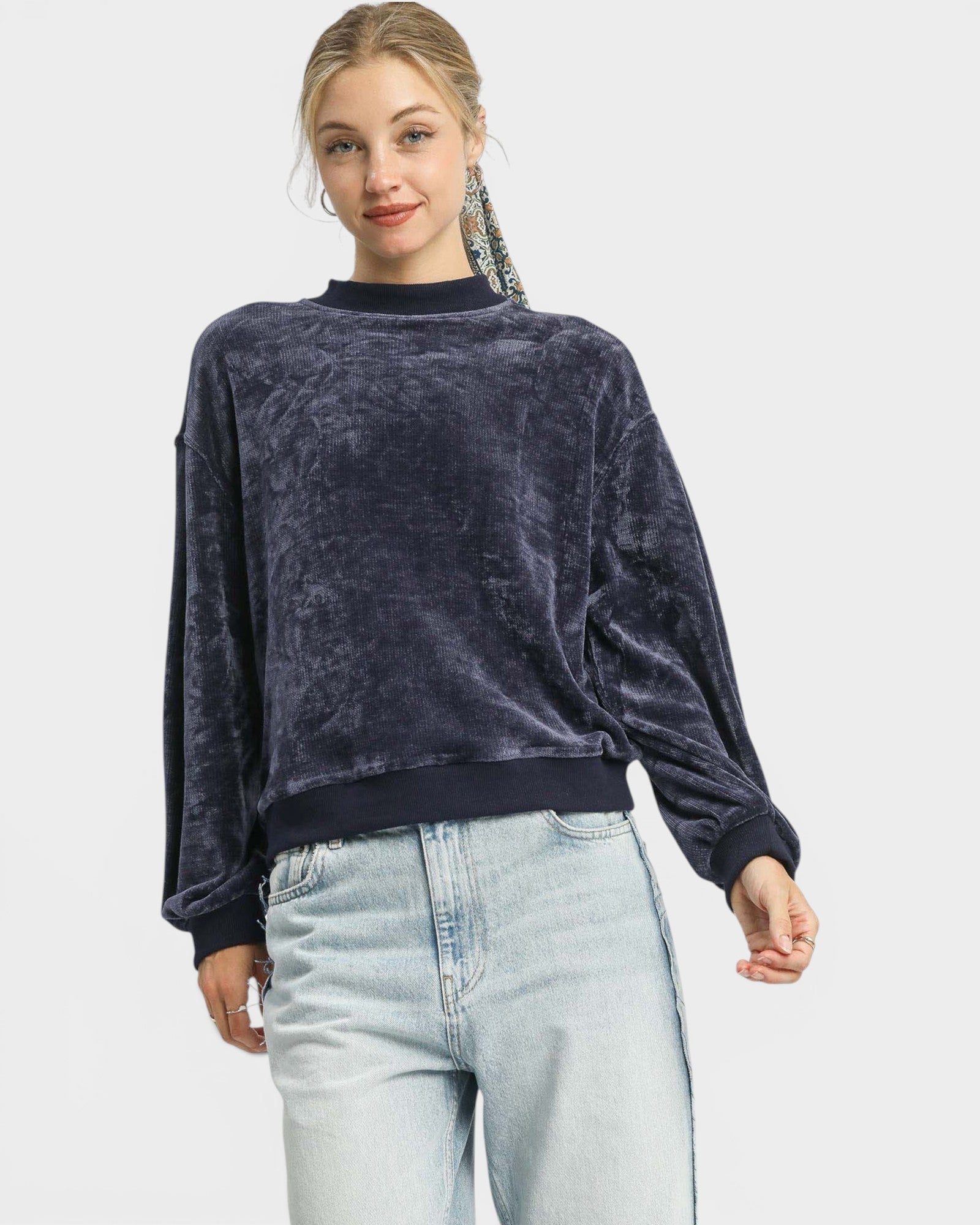 Woman wearing a dark blue velour sweater and light blue jeans on a white background