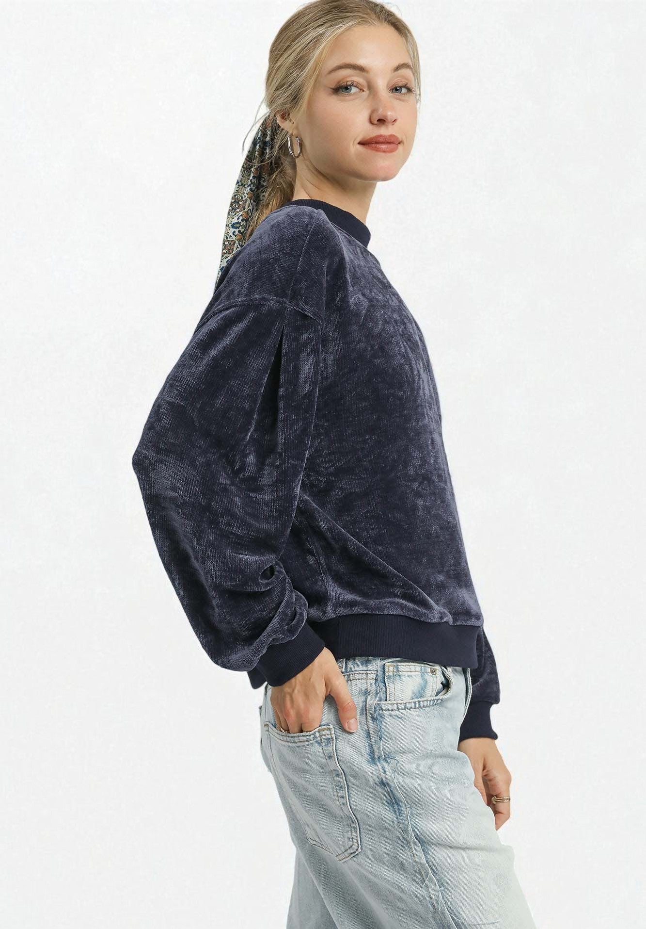 Woman wearing a dark blue velour sweatshirt and light blue jeans on a white background