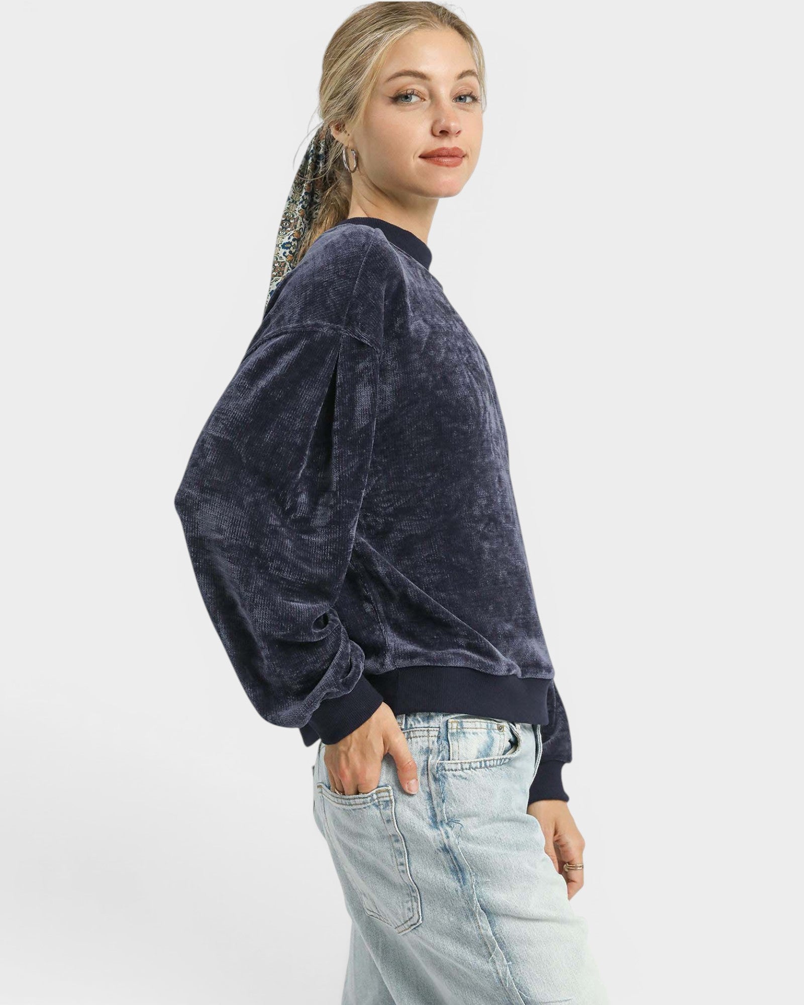 Person wearing a dark blue velour sweatshirt and light blue jeans on a white background