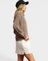Woman wearing a brown oversized sweater and white shorts on a plain background