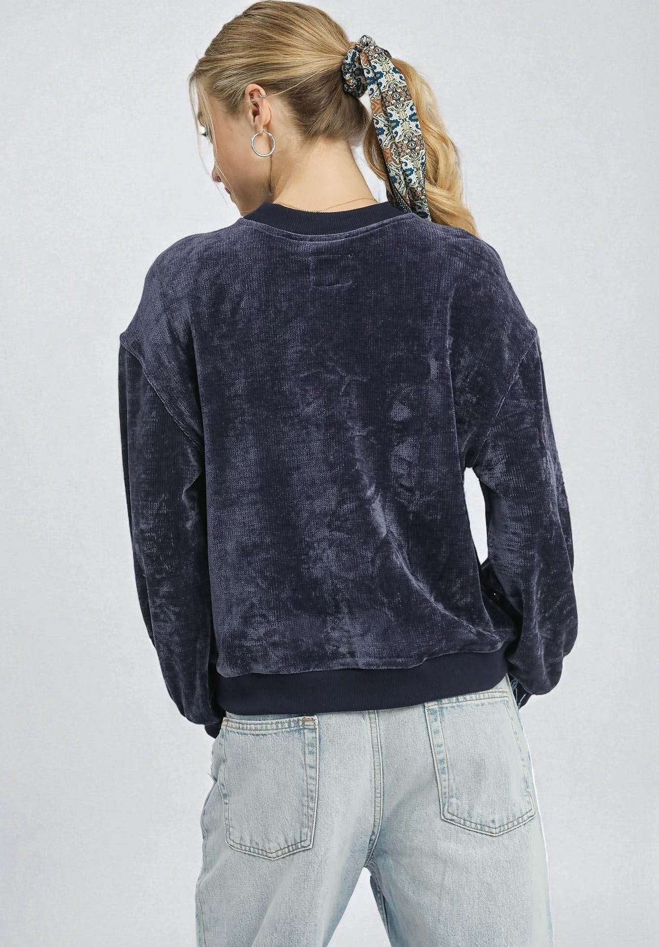 Person wearing a dark blue velour sweatshirt and light blue jeans on a plain background