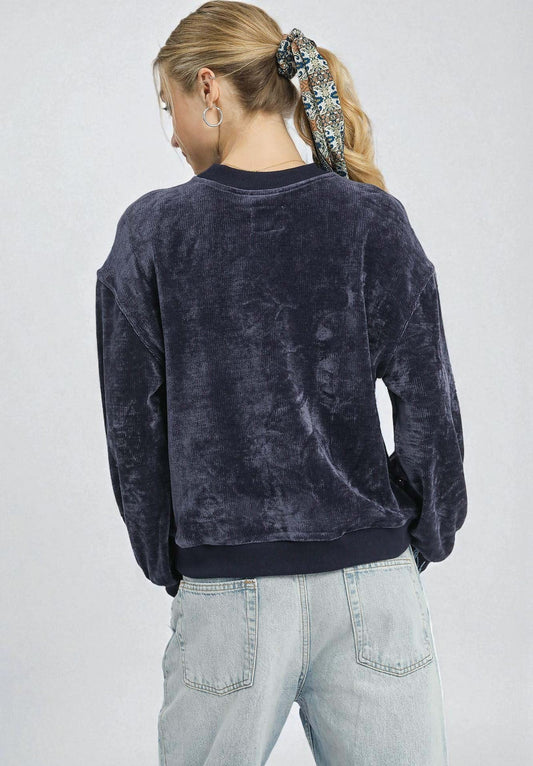 Person wearing a dark blue velour sweatshirt and light blue jeans on a plain background