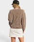 Person wearing a brown sweatshirt and white skirt with a black cap on a light gray background