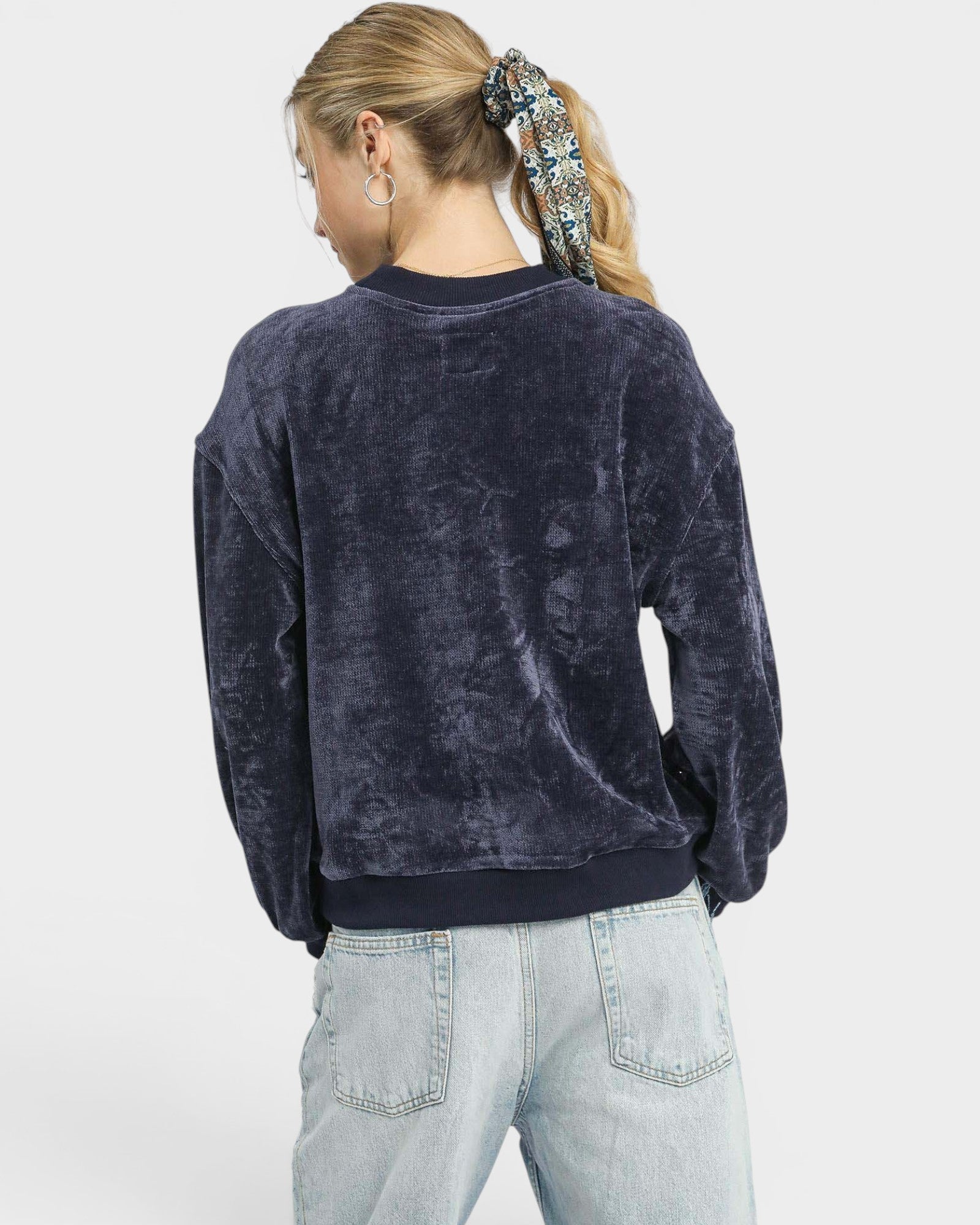 Person wearing a dark blue velour sweatshirt and light blue jeans on a white background
