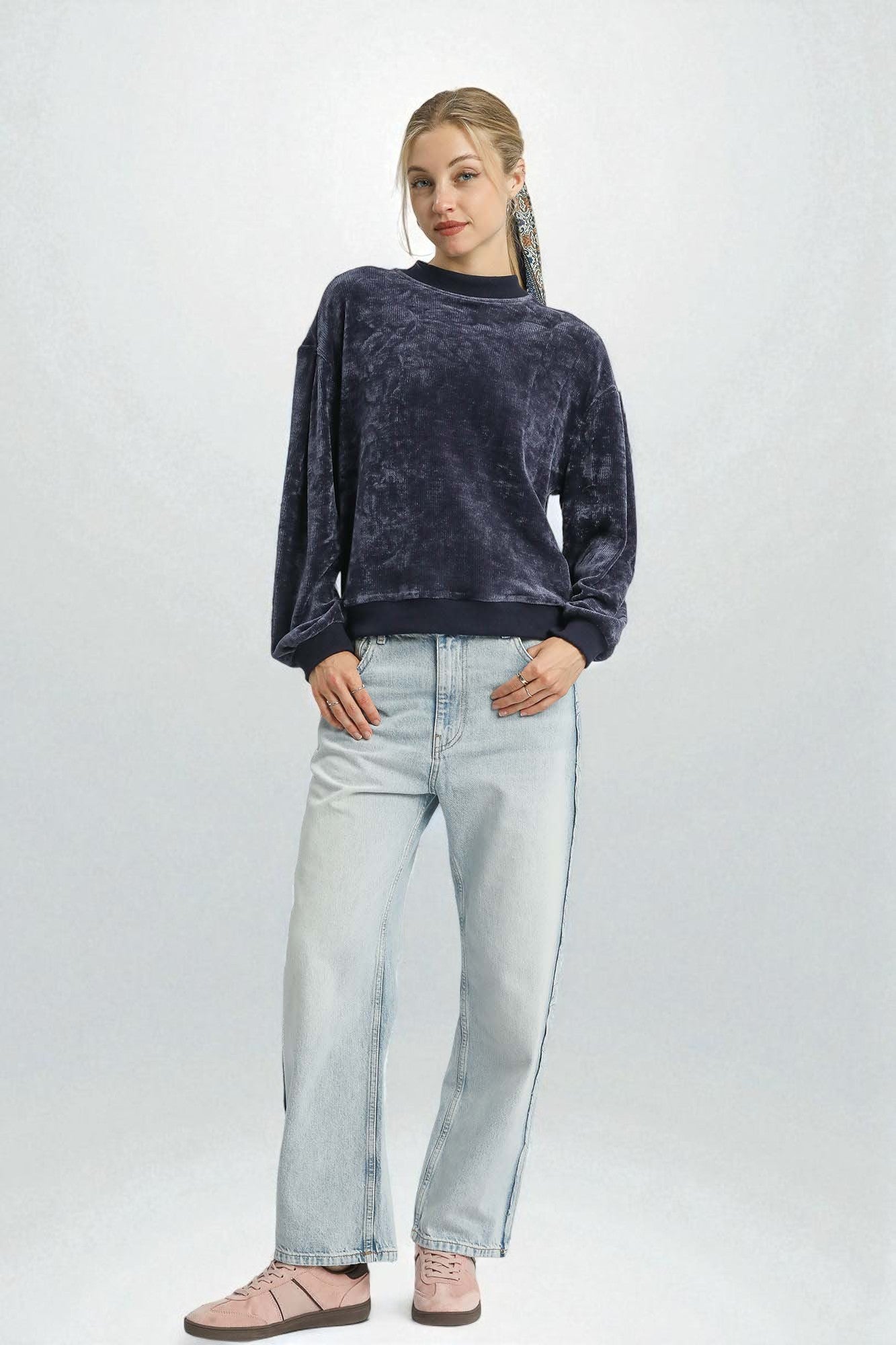 Woman wearing a dark blue velvet sweater and light blue jeans on a white background