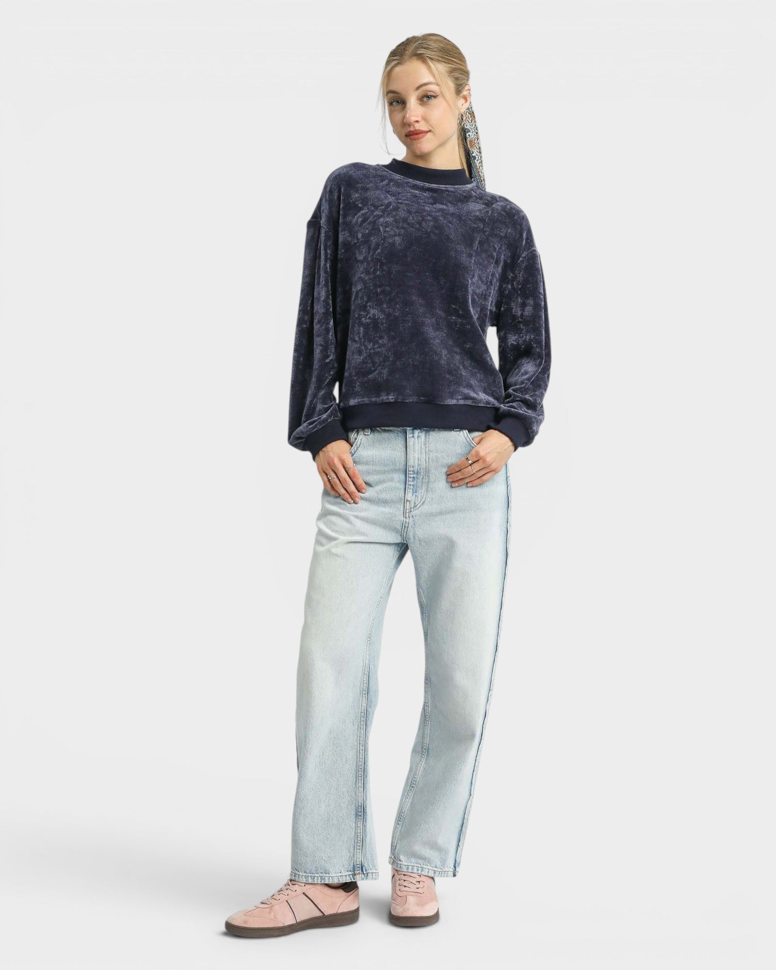 Woman wearing a dark blue textured sweater and light blue jeans on a white background