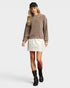 Woman wearing a brown sweatshirt, white skirt, and black boots on a plain background