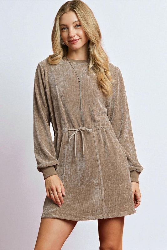 Woman wearing a brown corduroy dress with a plain background