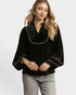 Woman wearing a black velvet blouse with gold trim on a white background
