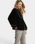 Woman wearing a black velvet top with gold trim and gray jeans on a white background