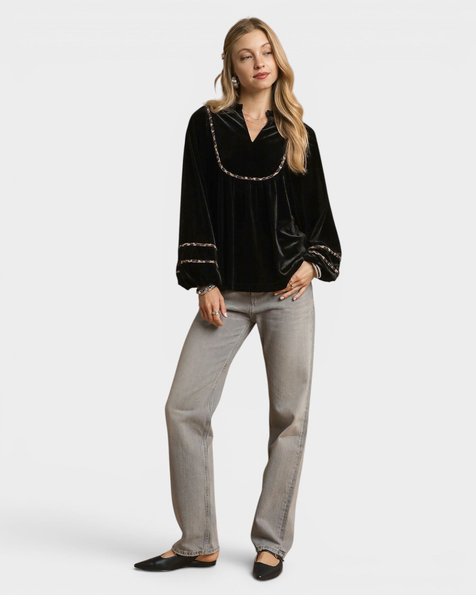 Woman wearing a black blouse with gold trim and gray pants on a white background