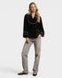 Woman wearing a black blouse with gold trim and gray pants on a white background