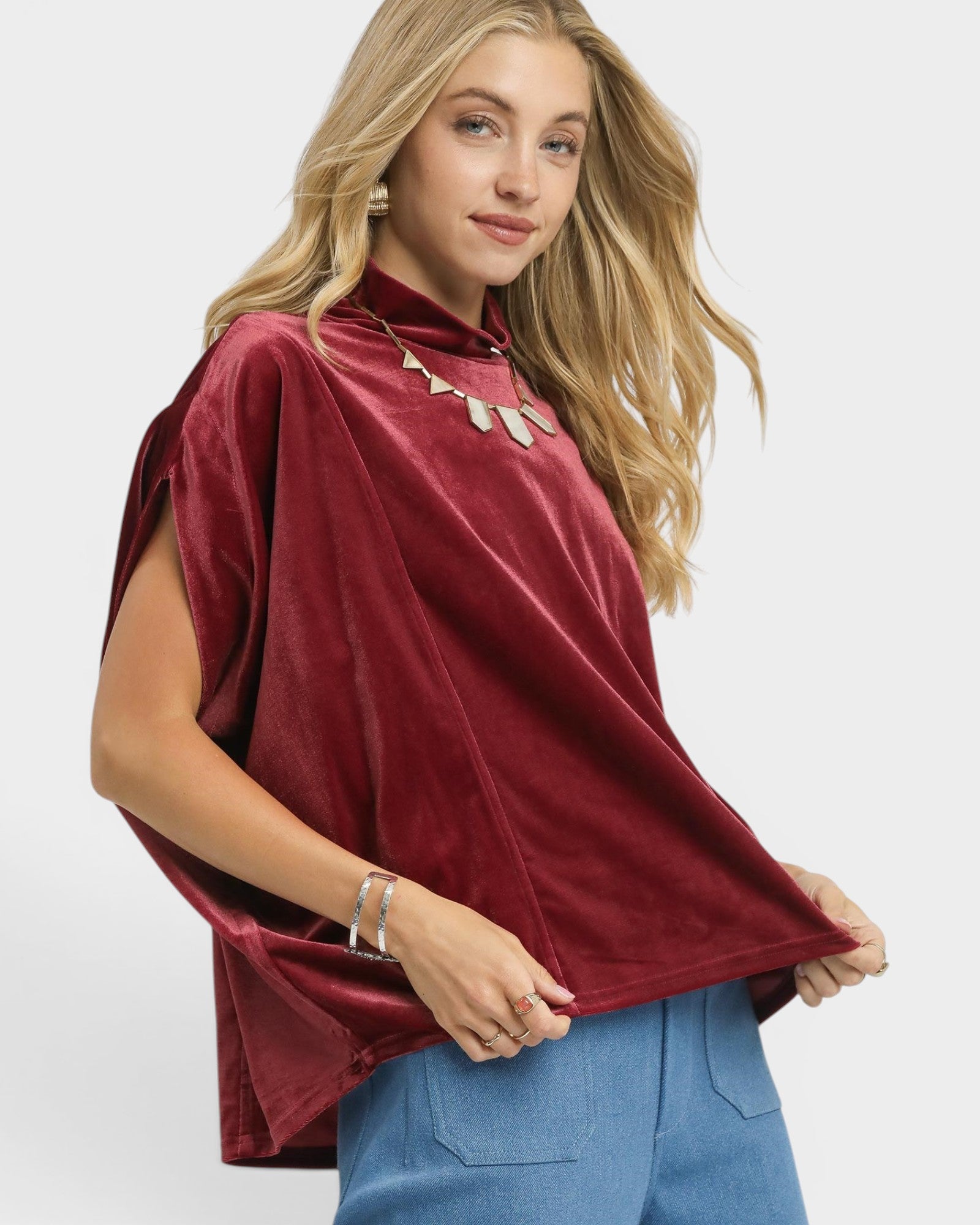 Woman wearing a burgundy top with a high collar and blue pants on a white background