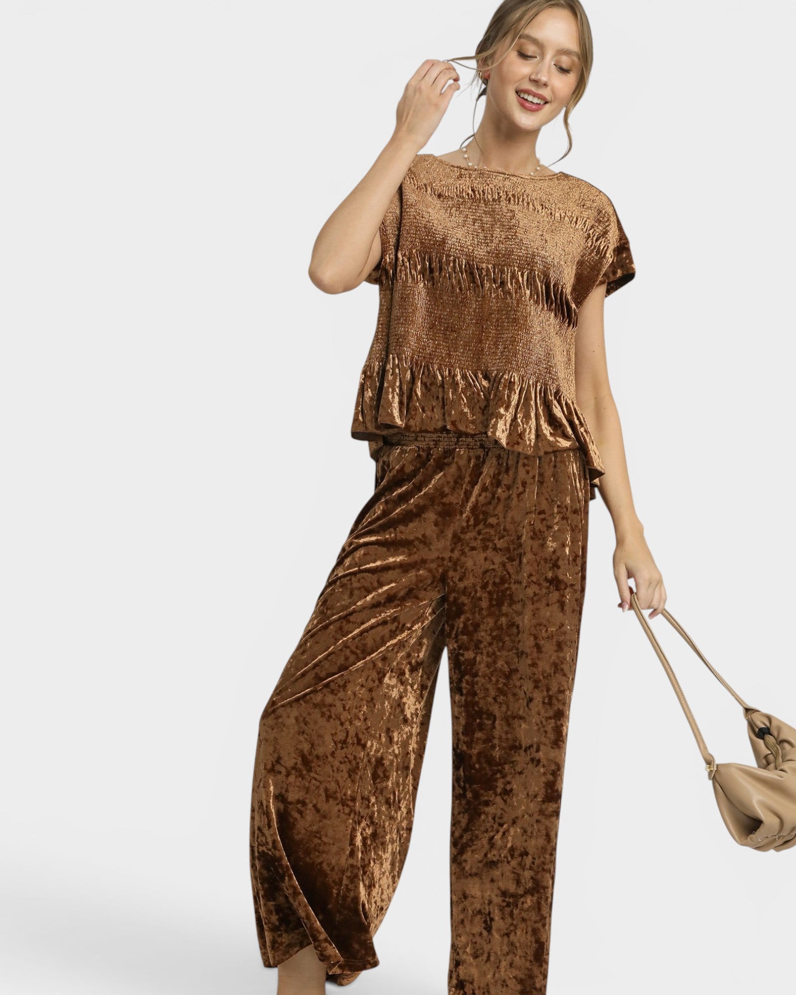 Woman wearing a brown velvet outfit with a matching handbag on a white background