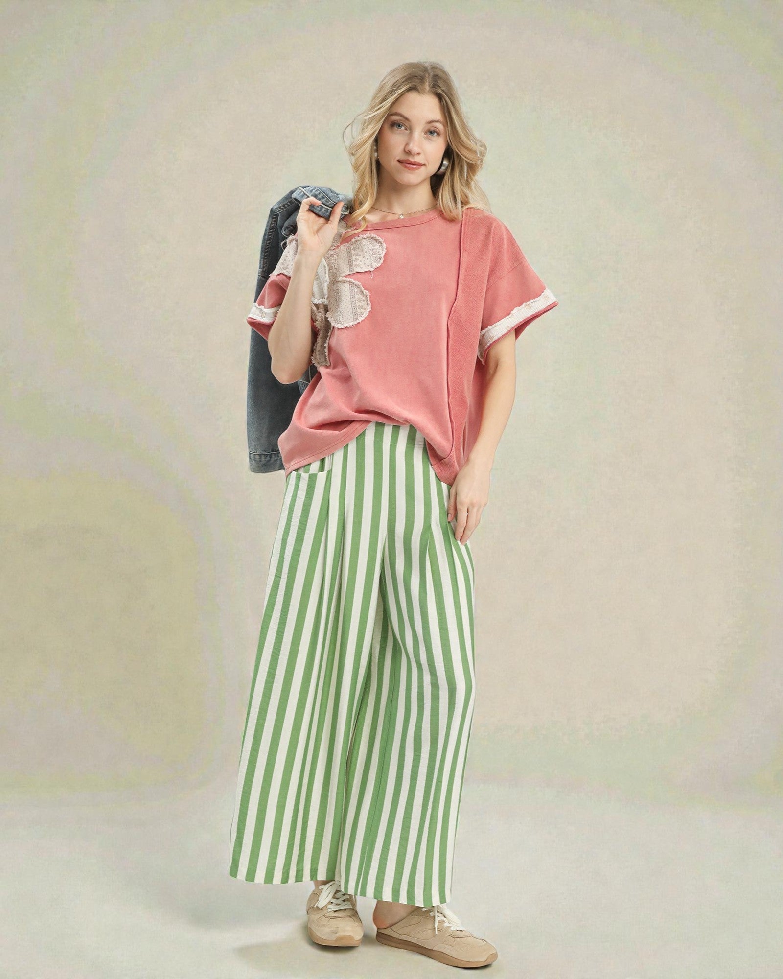 Woman wearing a pink top and green striped pants against a neutral background