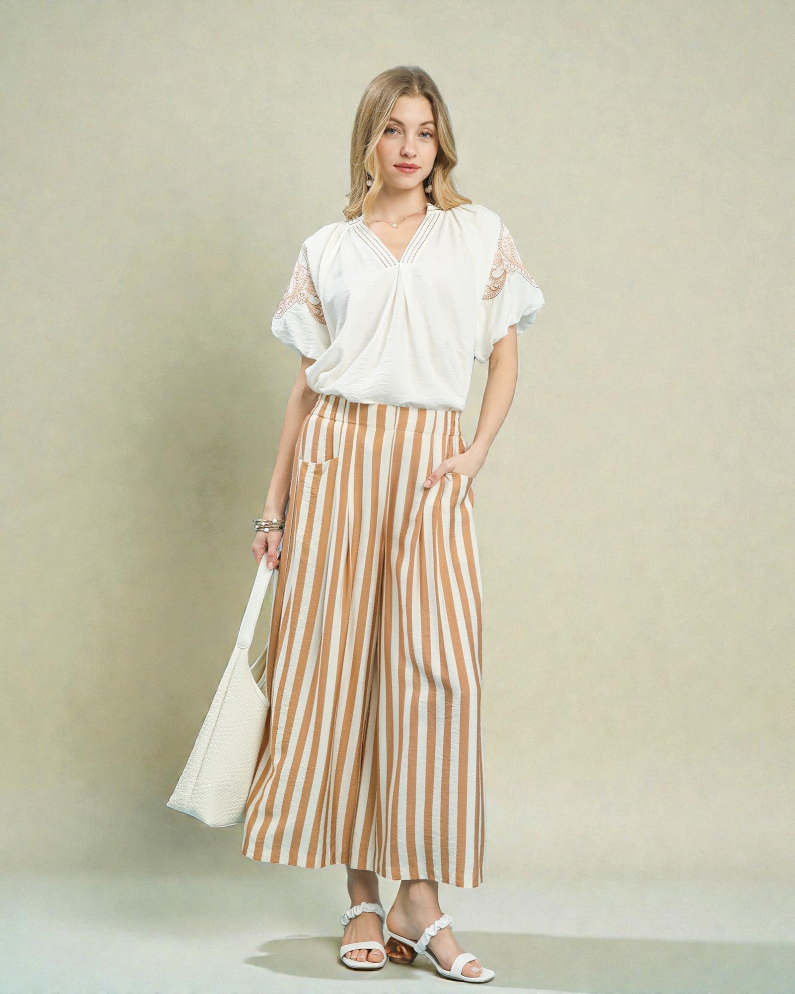 Woman wearing a white top and striped pants against a plain background