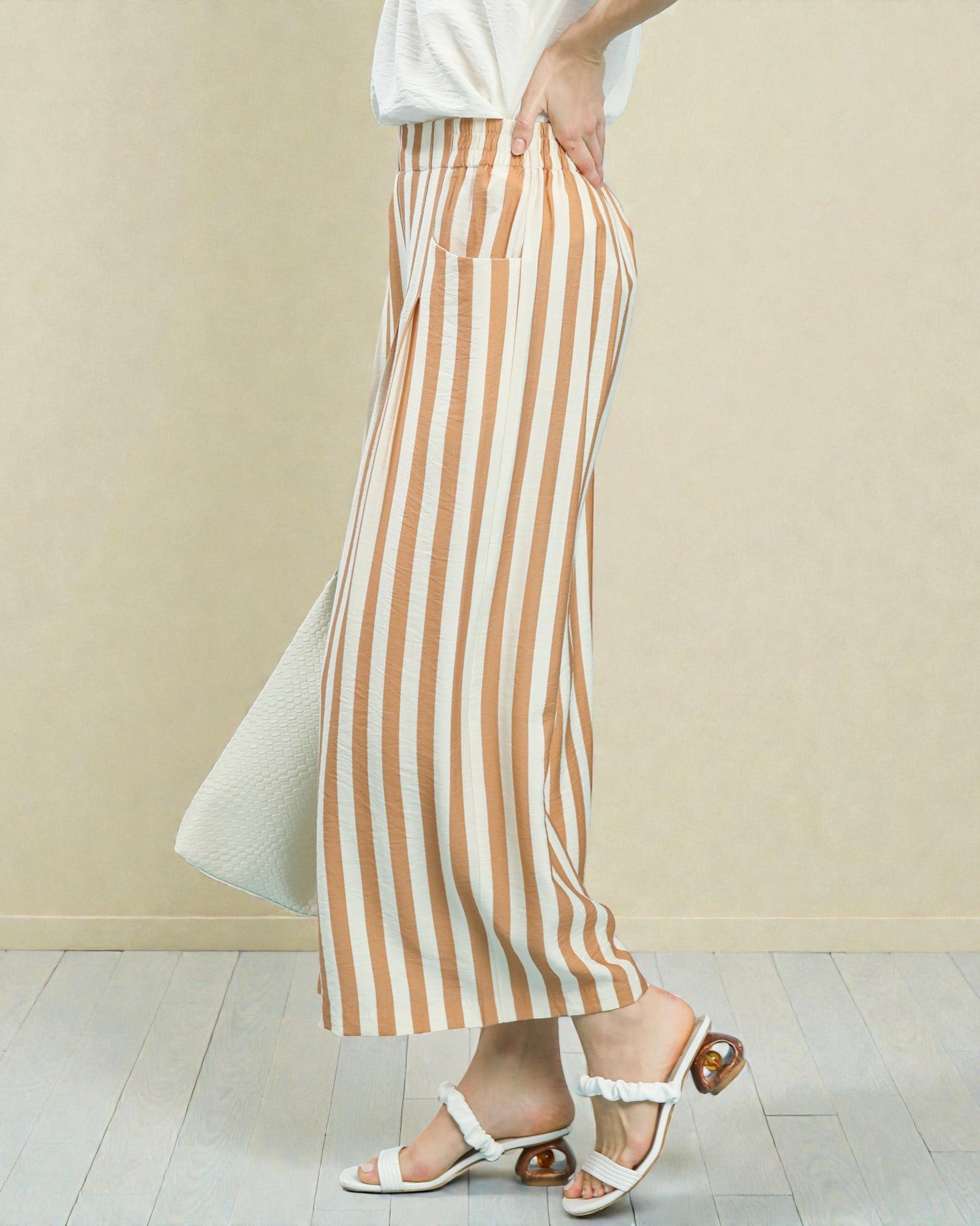 Person wearing brown and white striped pants against a beige background