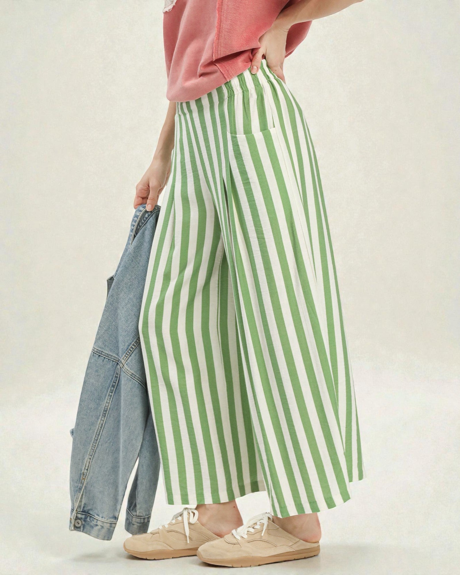 Person wearing green and white striped pants with a pink top and beige shoes on a light background
