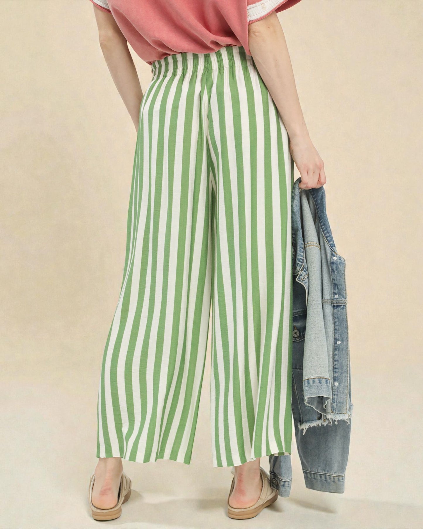 Person wearing green and white striped pants with a pink top and beige background