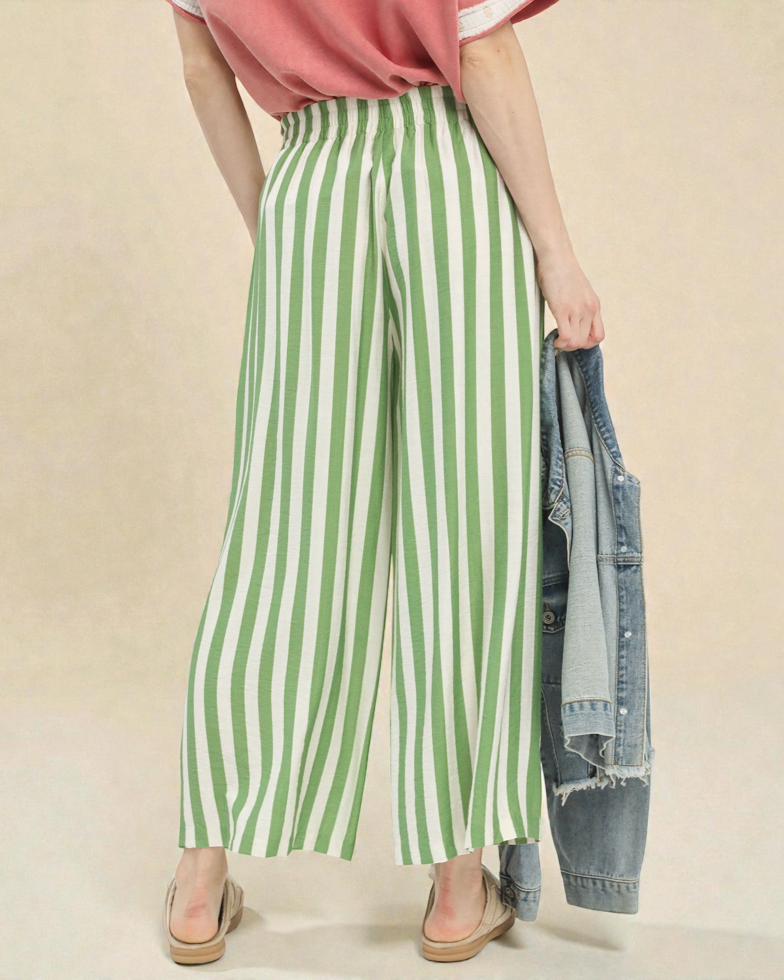 Person wearing green and white striped pants with a pink top and beige background