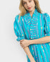Woman wearing a turquoise dress with colorful patterns on a white background