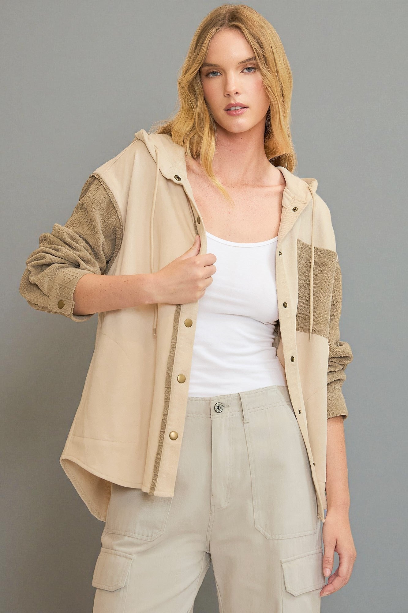 Woman wearing a beige jacket with a white top and light pants on a gray background