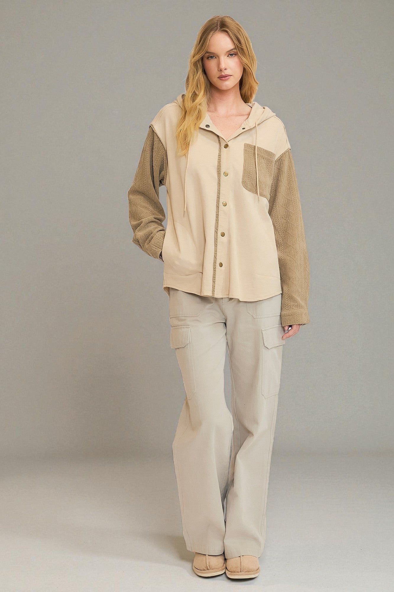 Woman wearing a beige and brown jacket with matching pants on a gray background
