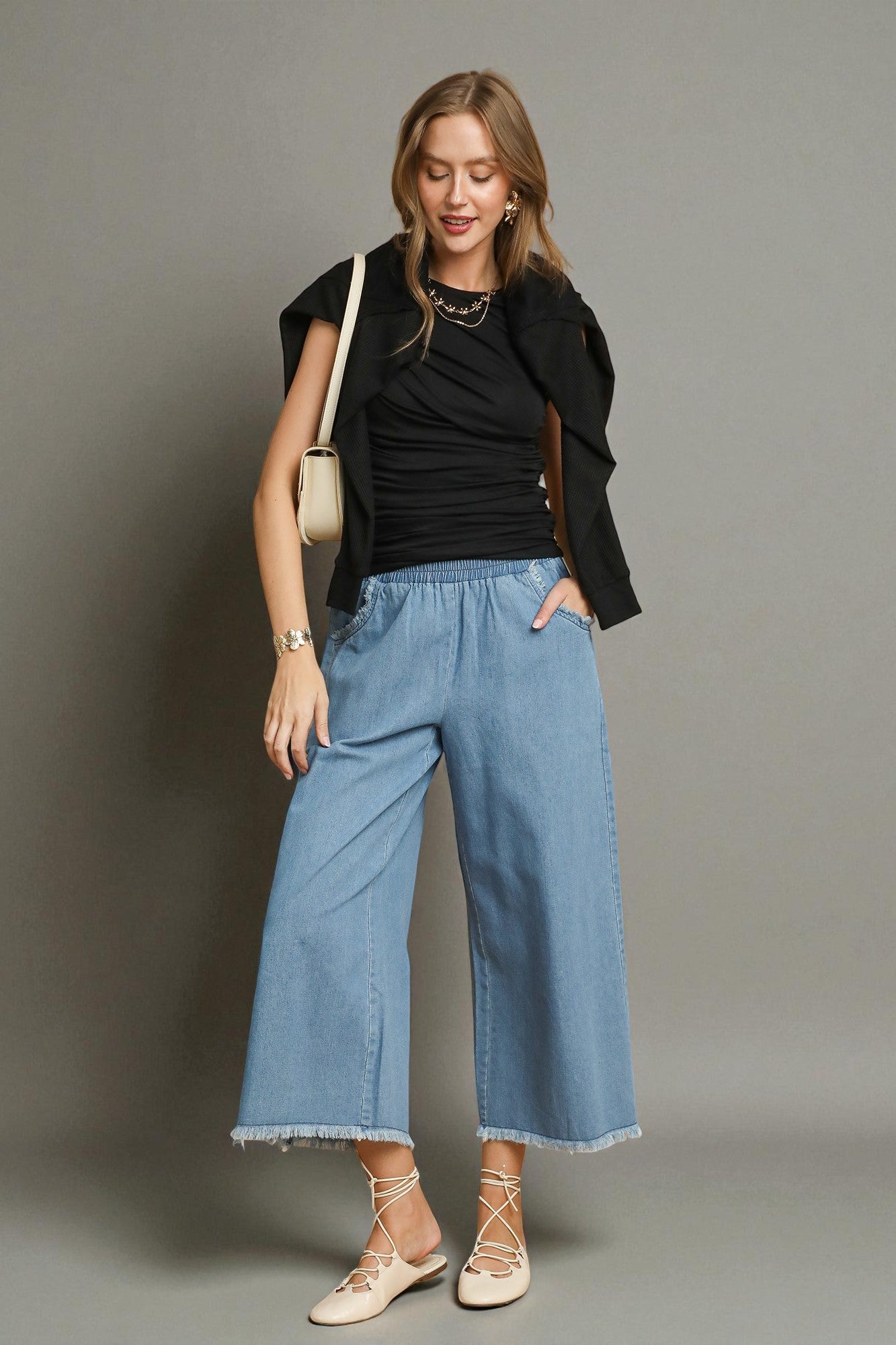 Woman wearing a black top, blue jeans, and beige shoes against a gray background