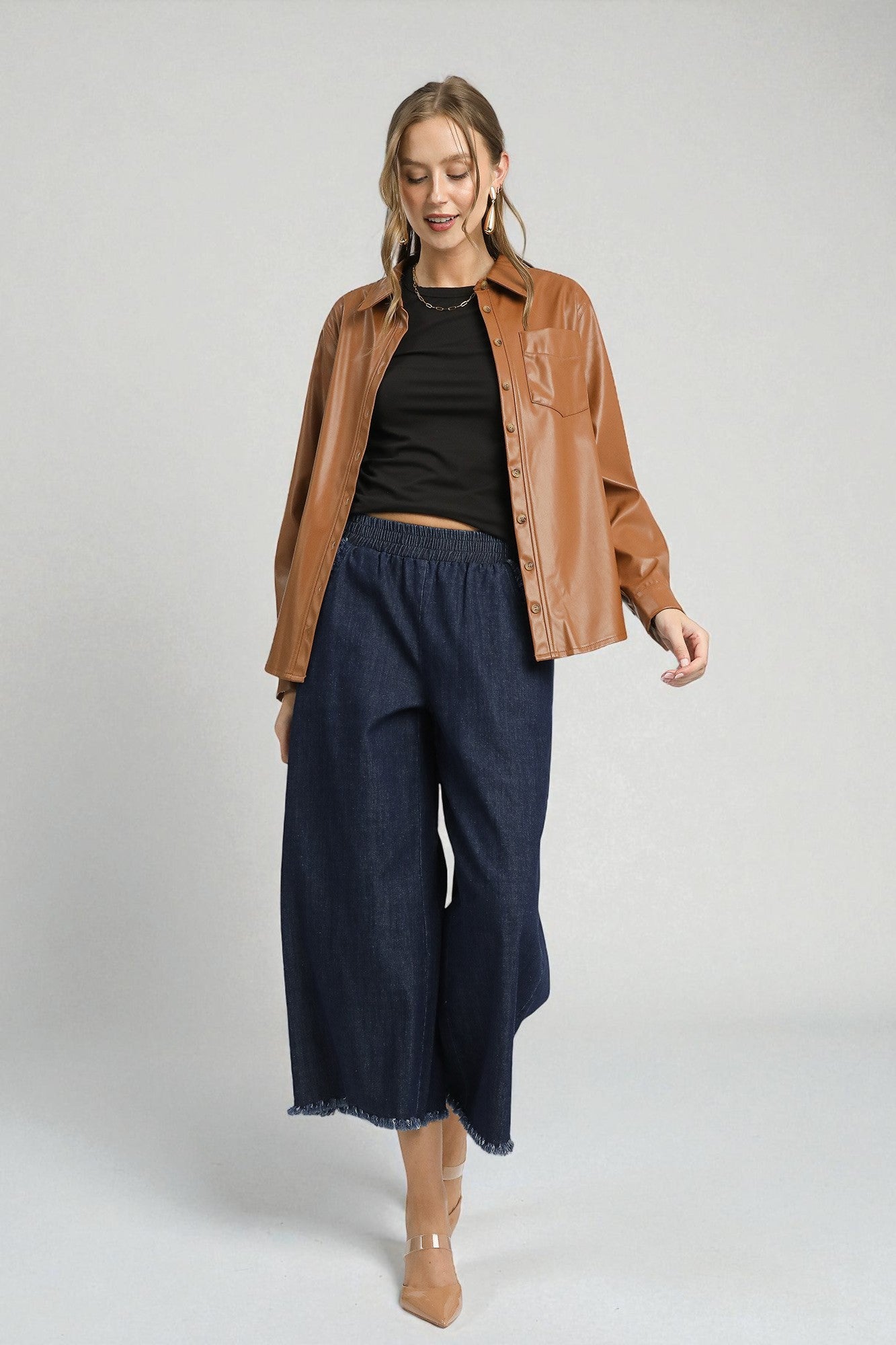 Woman wearing a brown jacket, black top, and blue pants on a white background