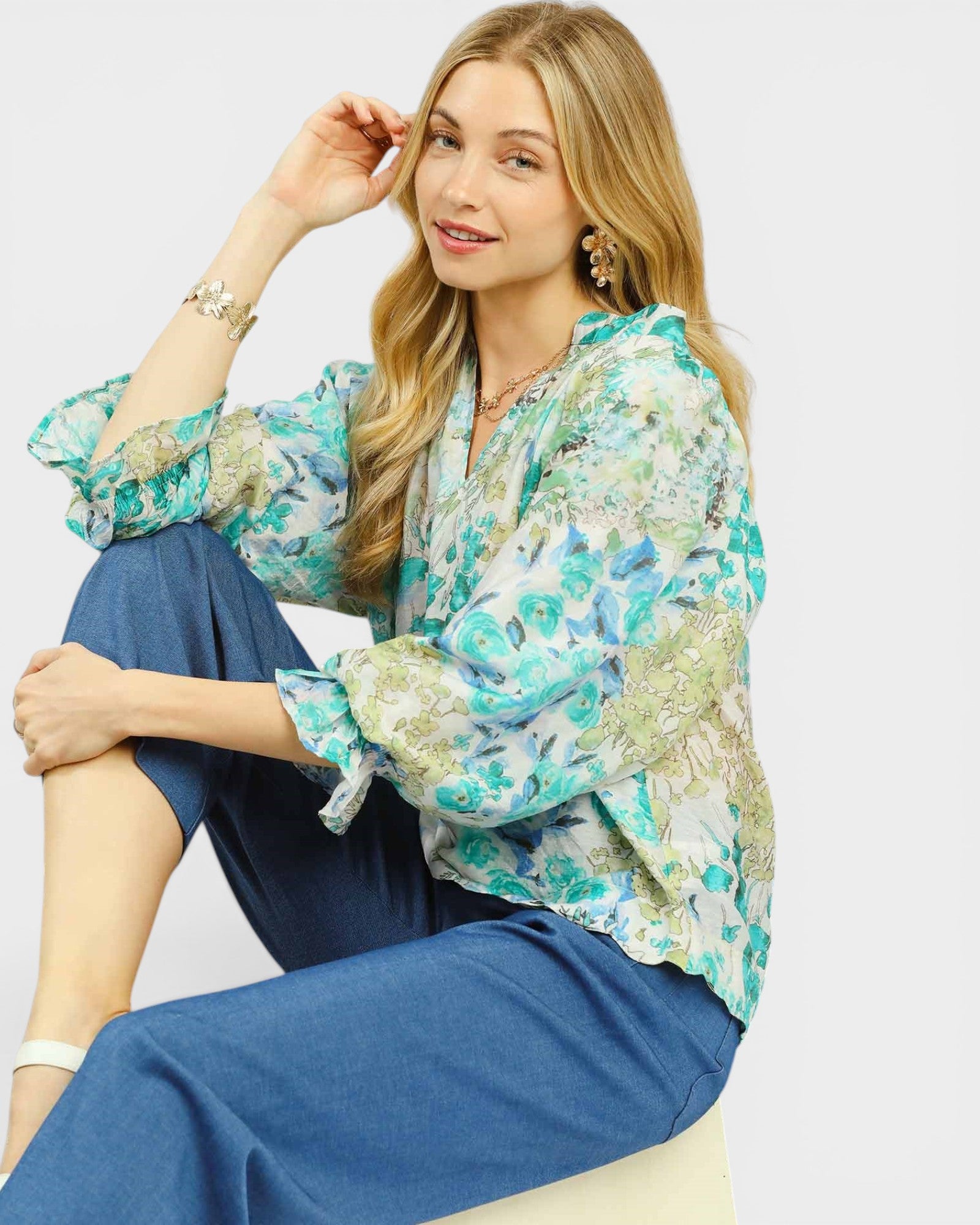 Woman wearing a floral blouse and blue pants sitting on a white surface.