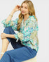 Woman wearing a floral blouse and blue pants sitting on a white surface.