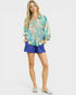 Woman wearing a floral blouse and blue shorts on a white background