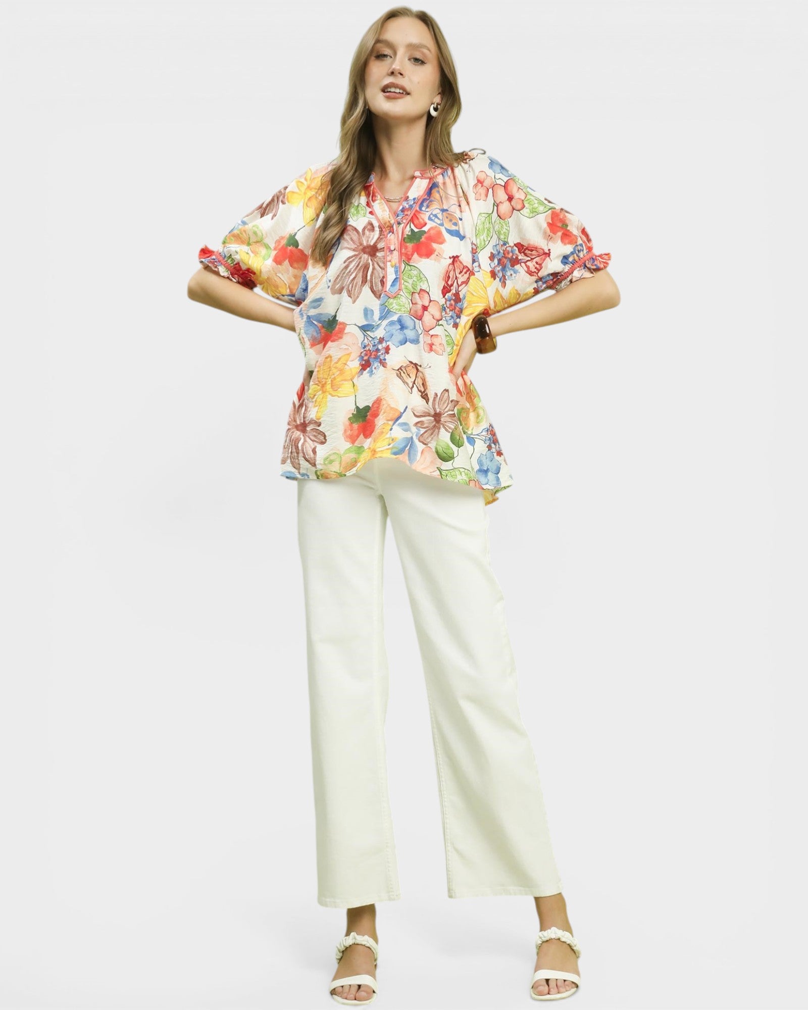 Woman wearing a colorful floral blouse and white pants on a white background
