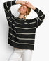 A woman wearing a black knit sweater with horizontal cream stripes and white pants, posing with her hands on her head against a plain white background.
