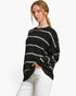 A woman wearing a black knit sweater with horizontal off-white stripes and white pants, photographed against a clean white studio background.