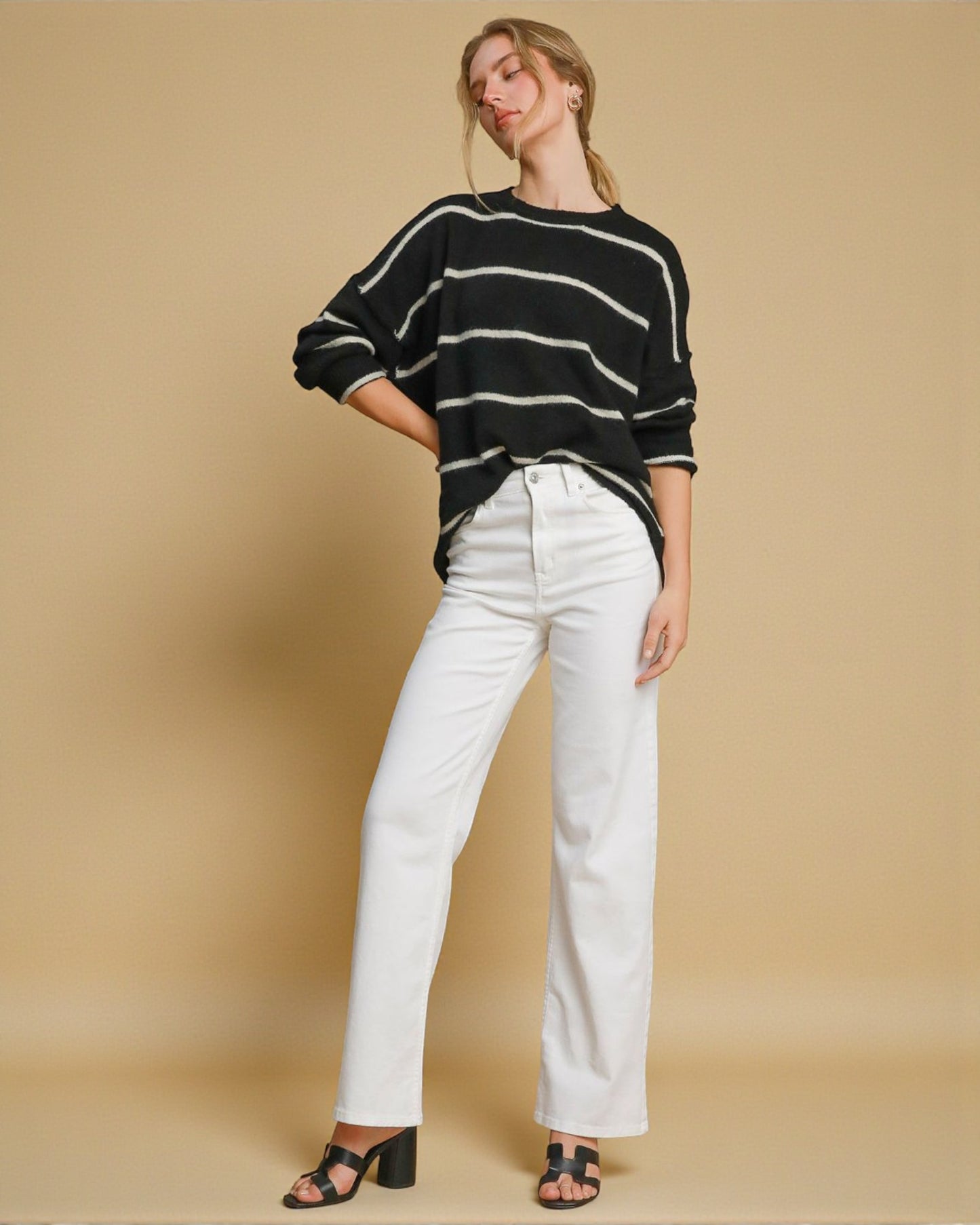 Woman wearing a black and white striped sweater and white pants on a beige background