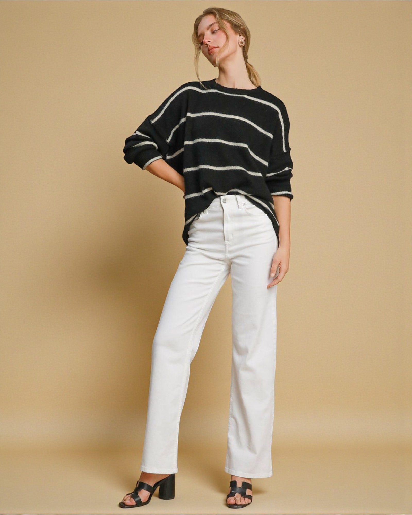 Woman wearing a black and white striped sweater and white pants on a beige background