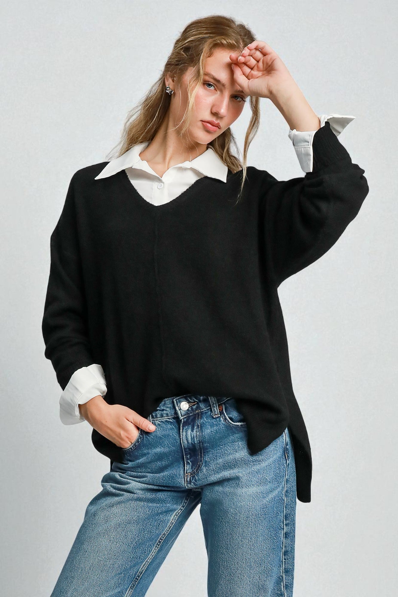 Woman wearing a black sweater with a white shirt underneath and blue jeans on a light gray background