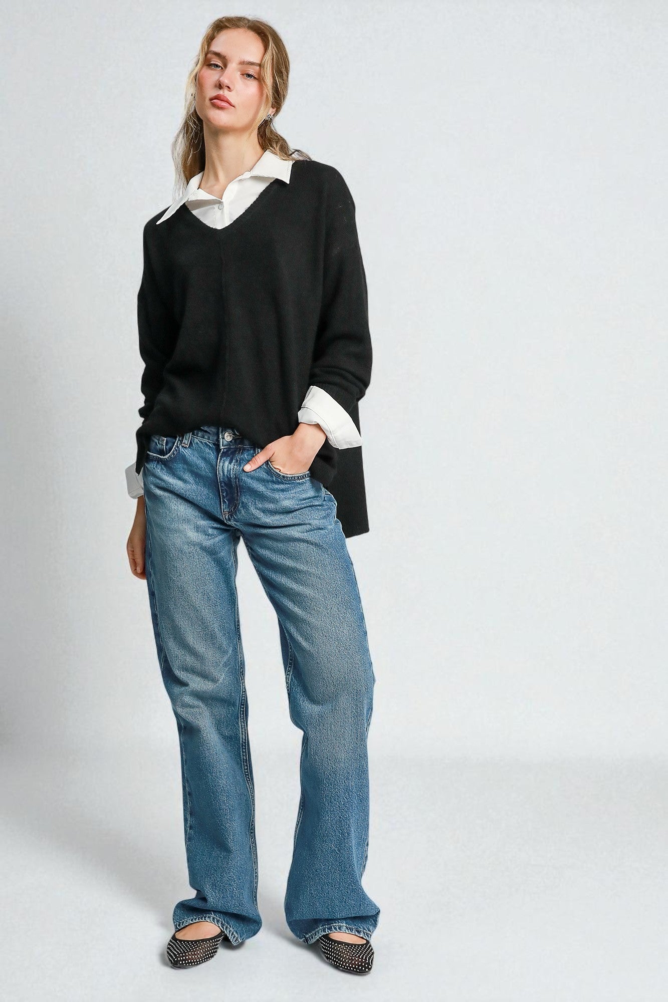 Person wearing a black sweater, white shirt, and blue jeans on a white background